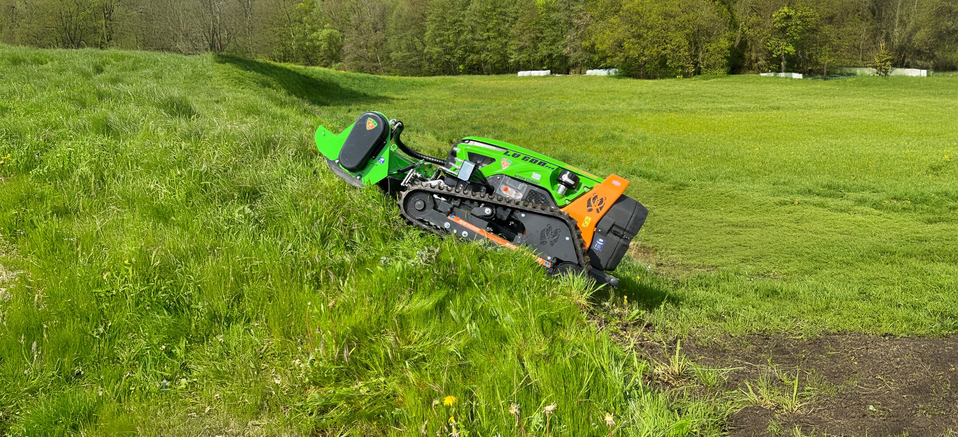 Grüne ferngesteuerte Mähraupe mäht steilen Wiesenhang bei der Landschaftspflege im Grünen.