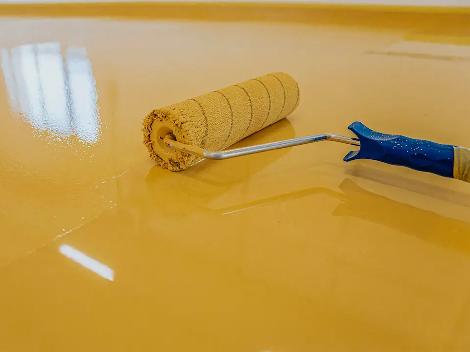 Eine Rolle verteilt eine frische Beschichtung auf einem glatten Bodenbelag.