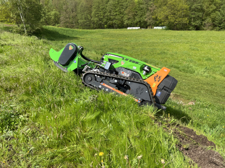 Grüne ferngesteuerte Mähraupe mäht steilen Wiesenhang bei der Landschaftspflege im Grünen.