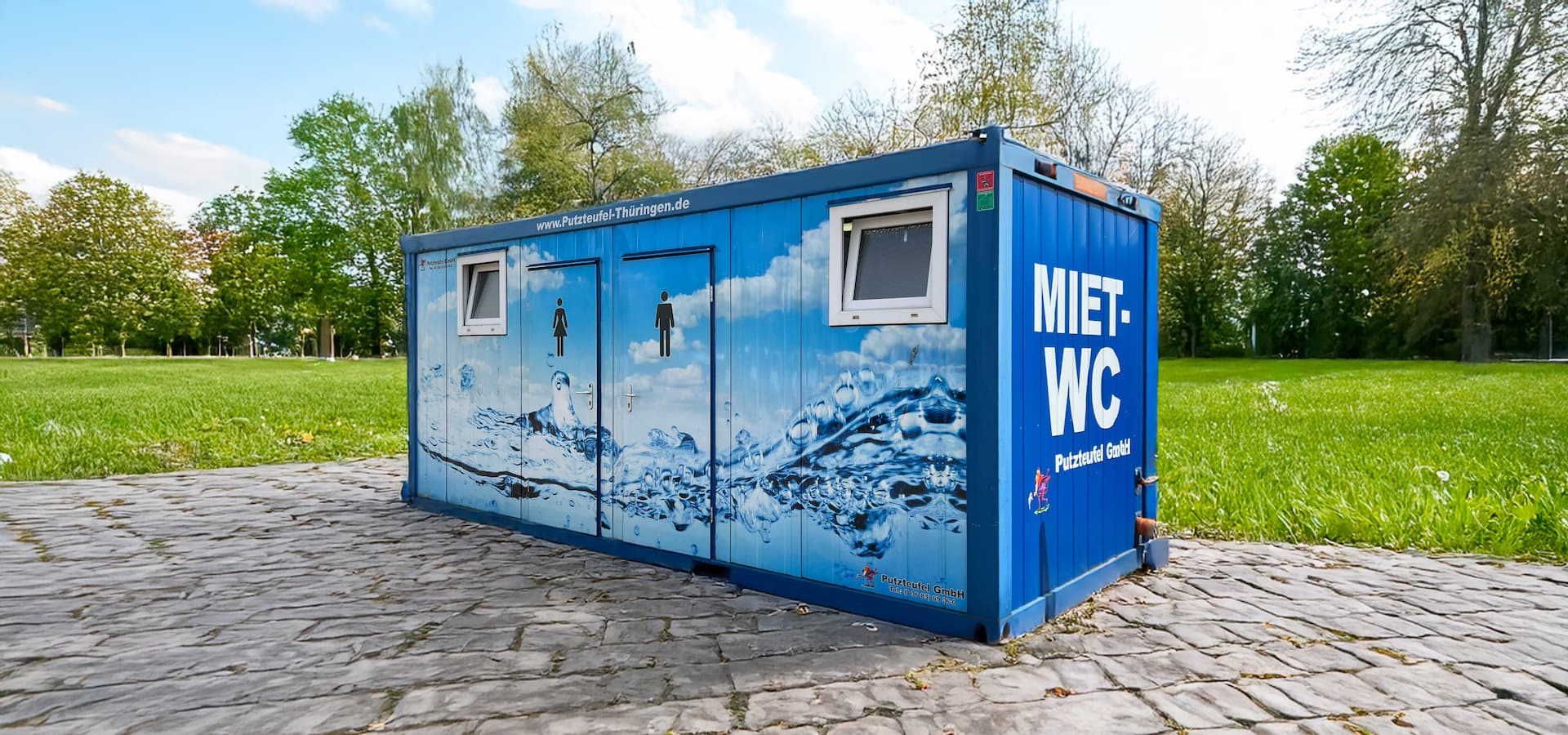 Blauer Miet-WC-Container der Putzteufel GmbH mit Wasserdesign und separaten Eingängen für Damen und Herren.