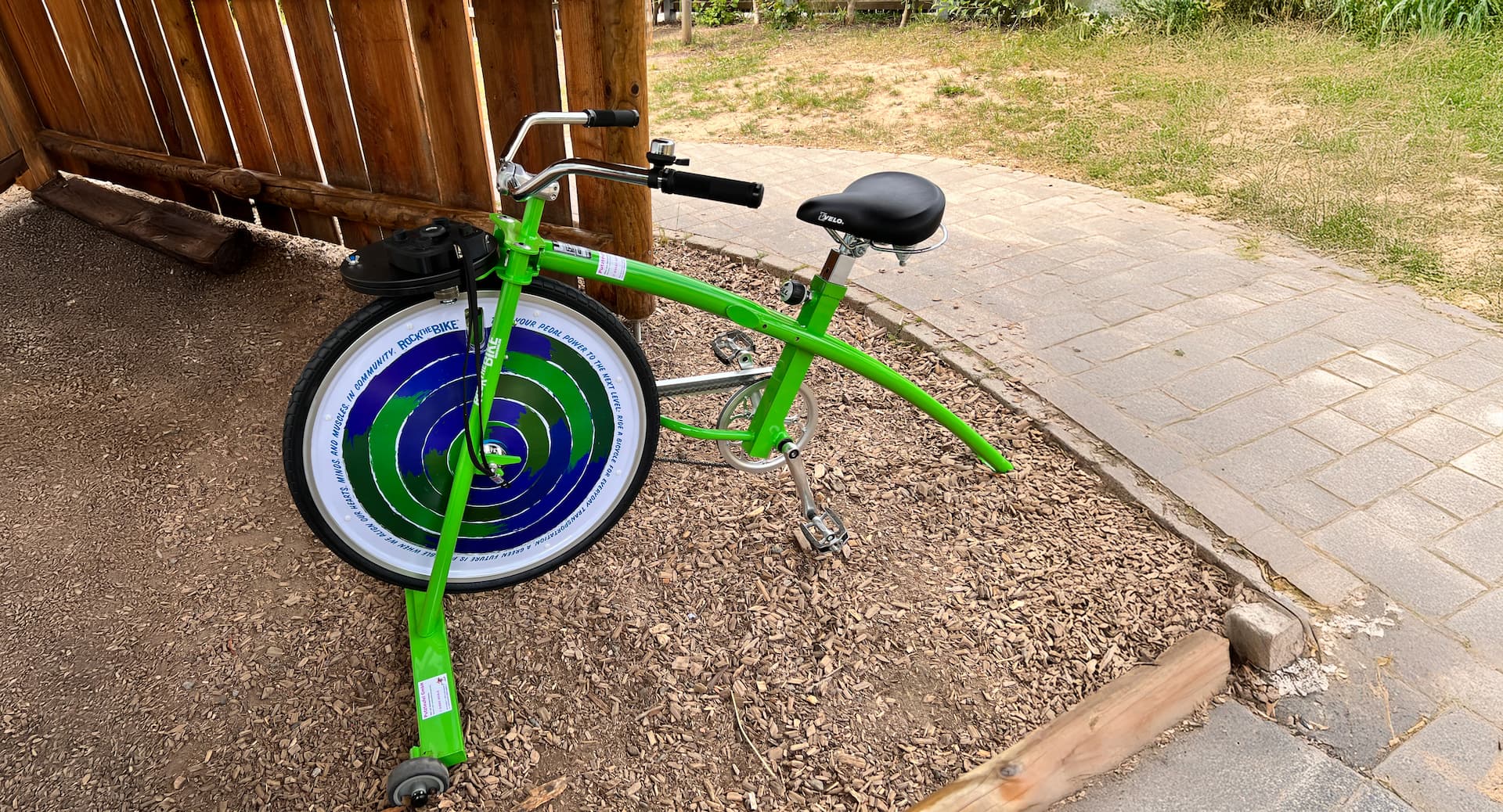 Grünes Smoothie-Bike mit Mixer, das durch Pedalkraft betrieben wird, steht auf Holzschnitzeln im Freien.