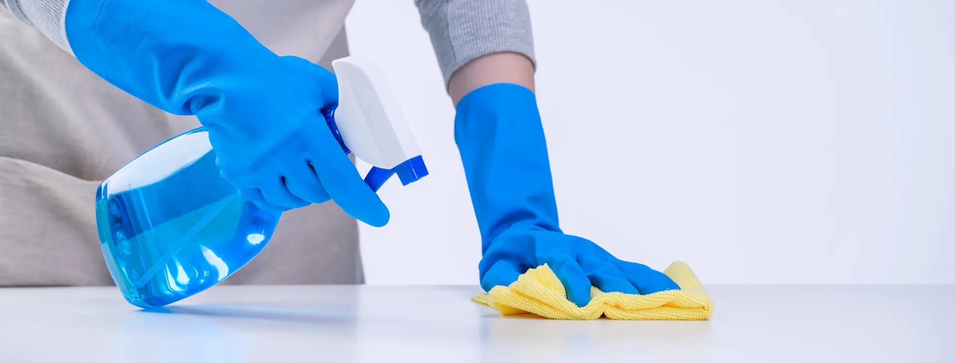 Reinigungskraft wischt Arbeitsfläche mit gelbem Tuch und Reinigungsspray.