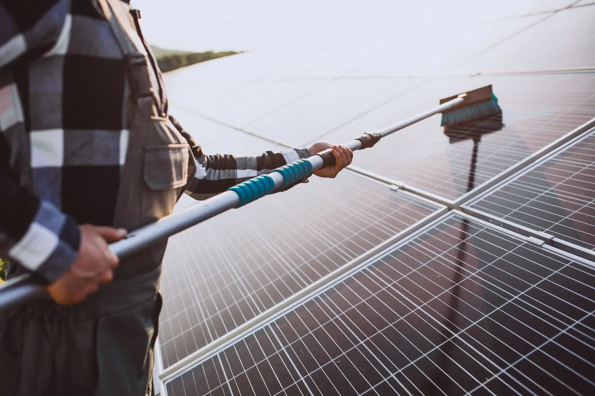 Fachkraft reinigt Solarpanels mit Teleskopbürste für optimale Leistung.
