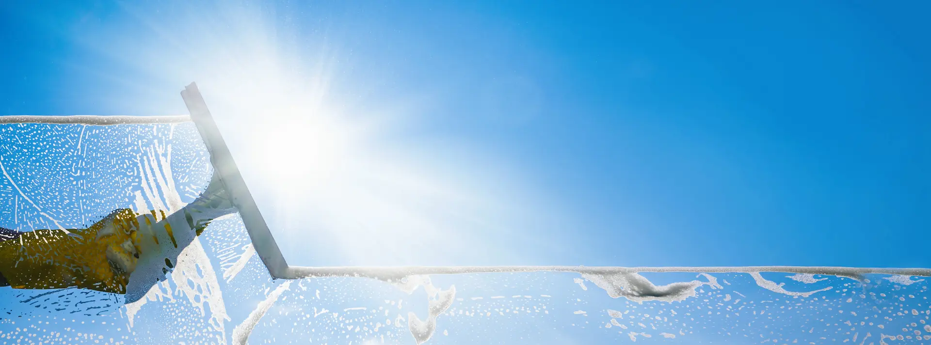 Reinigungskraft reinigt eine große Glasfläche mit einem Fensterabzieher vor blauem Himmel.