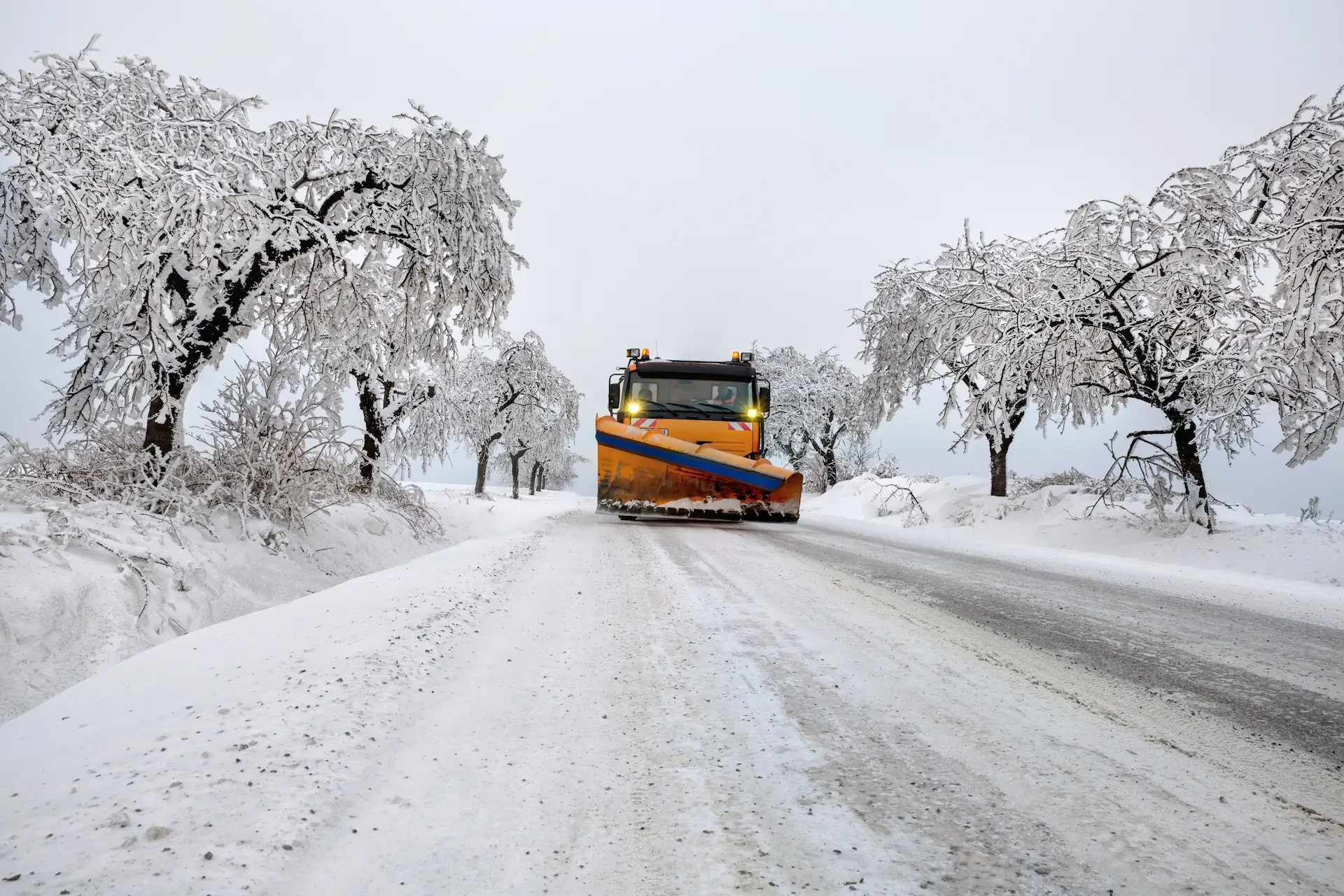 Räumfahrzeug entfernt Schnee von einer Straße in winterlicher Landschaft.
